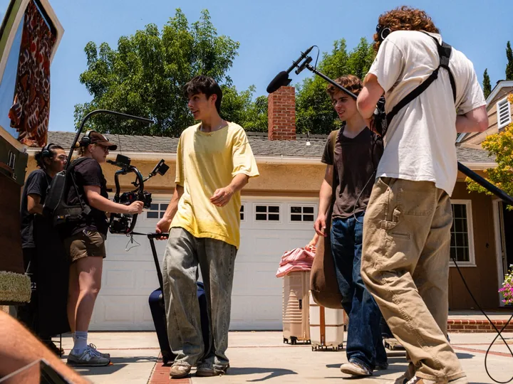 Cast and camera crew staging a sunny driveway scene with a boom microphone overhead